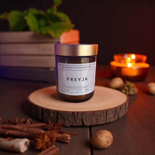 A candle in an amber container with a gold lid on a wooden table with various spices 