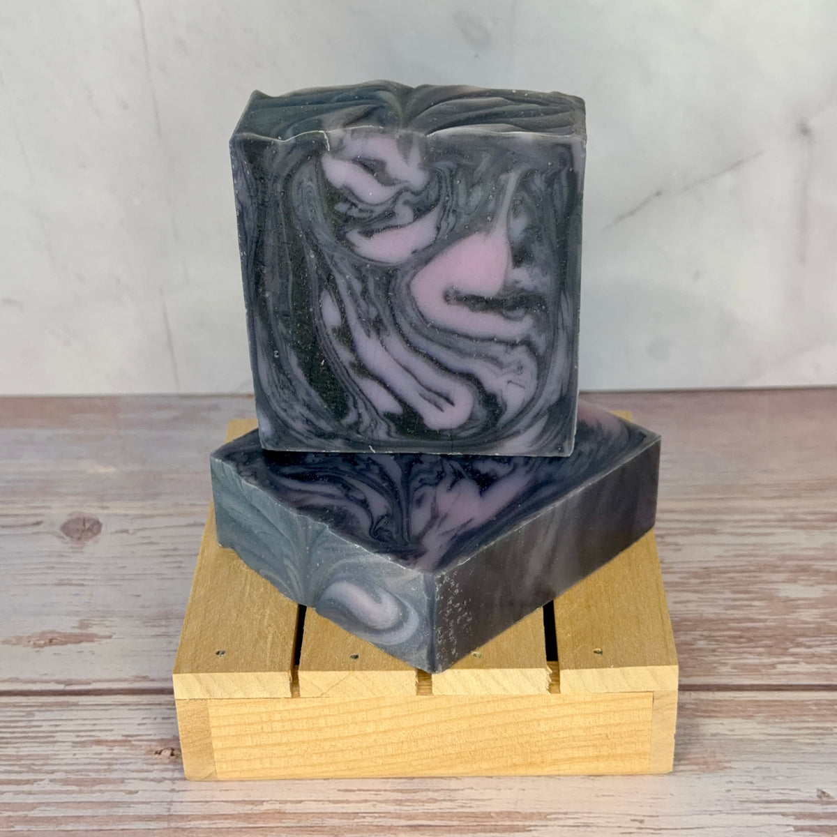 Marbled black and purple soap bar on a wooden soap dish with a neutral background